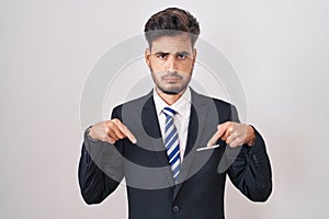 Young hispanic man with tattoos wearing business suit and tie pointing down looking sad and upset, indicating direction with