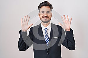 Young hispanic man with tattoos wearing business suit and tie showing and pointing up with fingers number ten while smiling