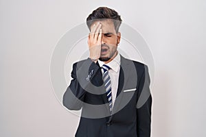 Young hispanic man with tattoos wearing business suit and tie yawning tired covering half face, eye and mouth with hand