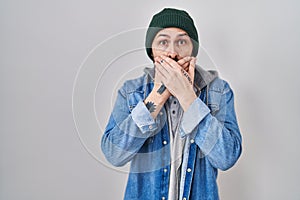 Young hispanic man with tattoos wearing wool cap shocked covering mouth with hands for mistake