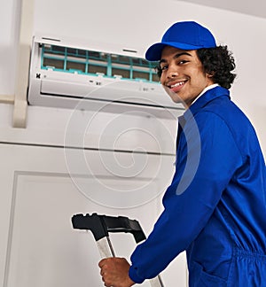 Young hispanic man technician repairing air conditioning at home