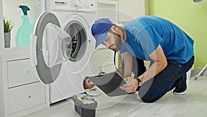 Young hispanic man technician repairing washing machine reading instructions at laundry room