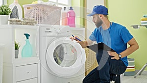 Young hispanic man technician repairing washing machine reading instructions at laundry room