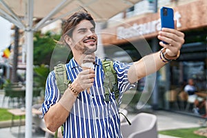 Young hispanic man tourist making selfie by smartphone eating ice cream at street