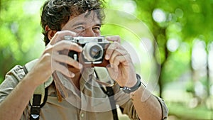 Young hispanic man tourist wearing backpack taking pictures with vintage camera walking away at park