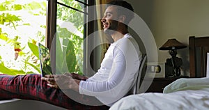 Young Hispanic Man Using Laptop Computer Happy Smiling Guy Chatting Online Over Big Window With Tropical Garden View