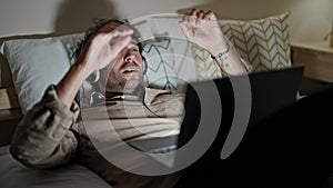 Young hispanic man using laptop and headphones relaxed on bed at bedroom
