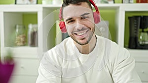 Young hispanic man using laptop and headphones sitting on table at dinning room