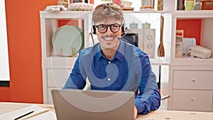 Young hispanic man using laptop and headphones sitting on table at dinning room