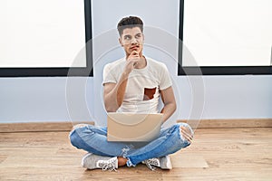 Young hispanic man using laptop at home thinking worried about a question, concerned and nervous with hand on chin