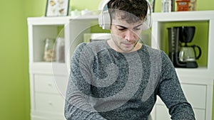 Young hispanic man using laptop sitting on the table wearing headphones at dinning room