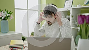 Young hispanic man using laptop wearing headphones at dinning room