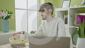Young hispanic man using laptop wearing headphones at dinning room
