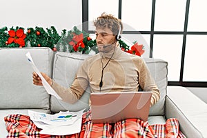 Young hispanic man using laptop working sitting by christmas decor at home