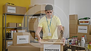 Young hispanic man volunteer packing clothes on cardboard box to donate at charity center