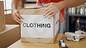 Young hispanic man volunteer packing clothes cardboard box to donate at charity center