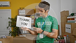 Young hispanic man volunteer pointing to thank you banner smiling at charity center
