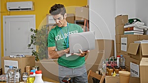 Young hispanic man volunteer using laptop checking products at charity center
