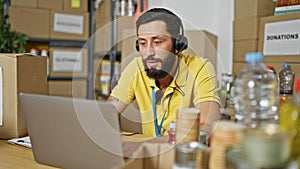 Young hispanic man volunteer using laptop and headphones at charity center