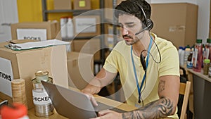 Young hispanic man volunteer using laptop and headphones at charity center