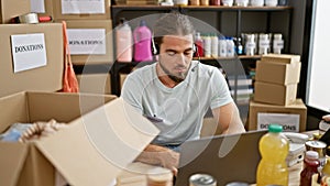 Young hispanic man volunteer using laptop and headphones at charity center