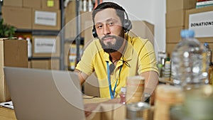 Young hispanic man volunteer using laptop and headphones at charity center