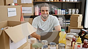 Young hispanic man volunteer using laptop and headphones smiling at charity center