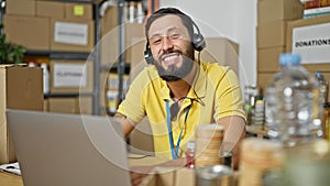 Young hispanic man volunteer using laptop and headphones smiling at charity center