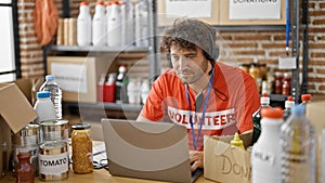 Young hispanic man volunteer using laptop and headphones working at charity center