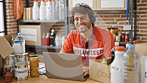 Young hispanic man volunteer using laptop and headphones working at charity center