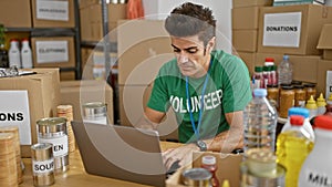 Young hispanic man volunteer using laptop with serious face at charity center