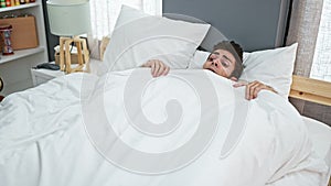 Young hispanic man waking up scared for nightmare at bedroom