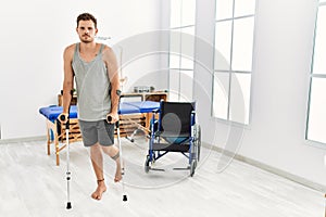 Young hispanic man walking using crutches at clinic