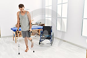 Young hispanic man walking using crutches at clinic