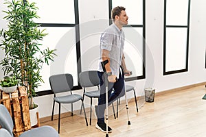 Young hispanic man walking using crutches at clinic waiting room