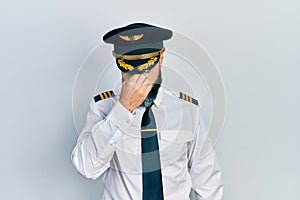 Young hispanic man wearing airplane pilot uniform tired rubbing nose and eyes feeling fatigue and headache