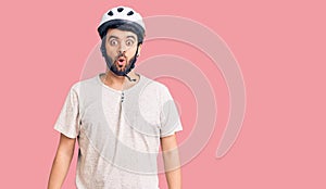 Young hispanic man wearing bike helmet scared and amazed with open mouth for surprise, disbelief face