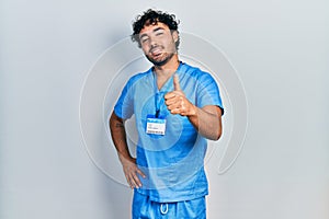 Young hispanic man wearing blue male nurse uniform doing happy thumbs up gesture with hand