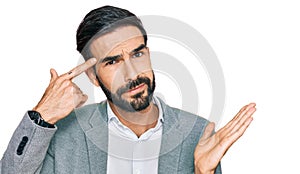 Young hispanic man wearing business clothes confused and annoyed with open palm showing copy space and pointing finger to forehead
