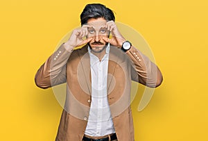 Young hispanic man wearing business clothes trying to open eyes with fingers, sleepy and tired for morning fatigue