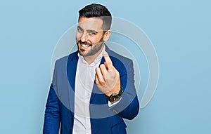 Young hispanic man wearing business jacket beckoning come here gesture with hand inviting welcoming happy and smiling