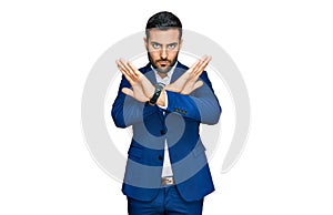 Young hispanic man wearing business jacket rejection expression crossing arms and palms doing negative sign, angry face