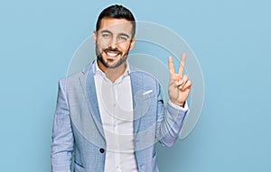 Young hispanic man wearing business jacket smiling with happy face winking at the camera doing victory sign