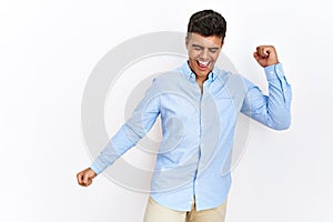 Young hispanic man wearing business shirt standing over isolated background dancing happy and cheerful, smiling moving casual and