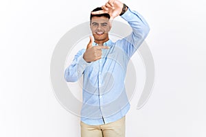 Young hispanic man wearing business shirt standing over isolated background smiling making frame with hands and fingers with happy