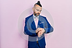 Young hispanic man wearing business suit and tie checking the time on wrist watch, relaxed and confident