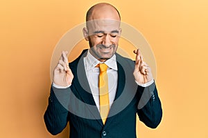 Young hispanic man wearing business suit and tie gesturing finger crossed smiling with hope and eyes closed