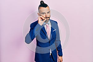 Young hispanic man wearing business suit and tie mouth and lips shut as zip with fingers