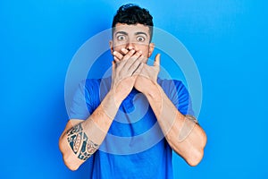 Young hispanic man wearing casual blue t shirt shocked covering mouth with hands for mistake