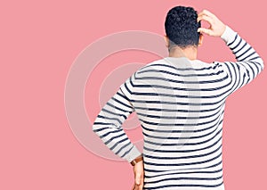 Young hispanic man wearing casual clothes backwards thinking about doubt with hand on head